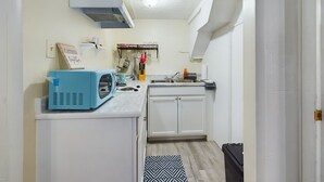 Cocina compacta con armarios blancos, un microondas azul y un colgador para ollas.