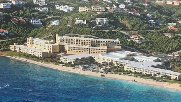 Un hôtel situé sur la côte, composé de plusieurs bâtiments, avec une plage et un paysage vallonné en arrière-plan.