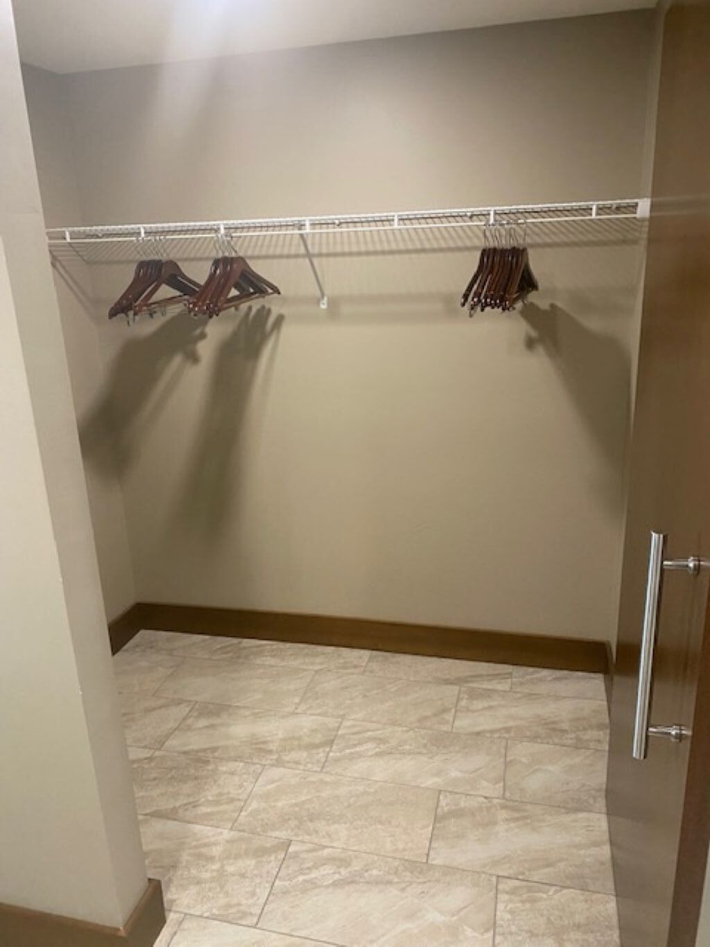 A walk-in closet with a metal rack for hanging clothes, a tiled floor, and a wooden door.