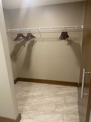 Un dressing accessible sans porte, doté d’une étagère en métal pour suspendre les vêtements, d’un sol carrelé et d’une porte en bois.