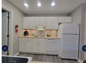 A modern kitchen with white cabinets, a white refrigerator, and a dishwasher. There are three ceiling lights, a coffee maker, and a fire extinguisher on the wall. - Cozy 2-bedroom apartment in charming Ocean City with AC (Ocean city)