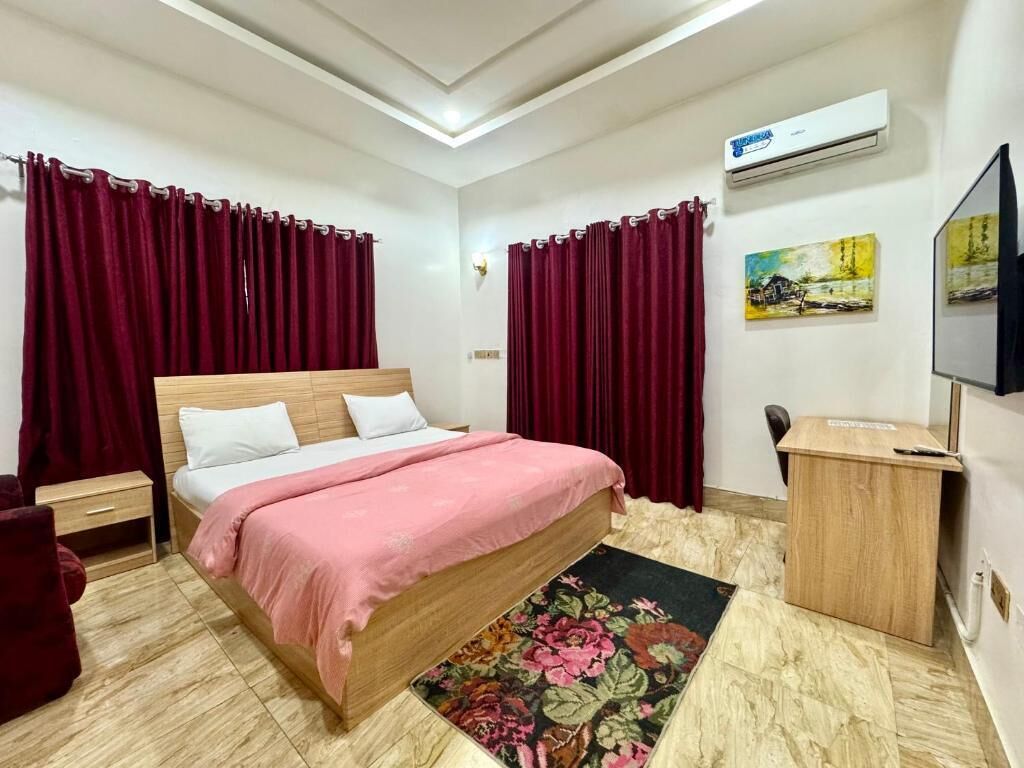 Un dormitorio con cama de madera, cortinas rojas, un escritorio y un televisor.