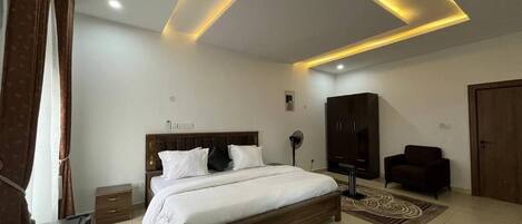 A modern bedroom with a large bed, a wardrobe, a desk, and a ceiling light fixture.