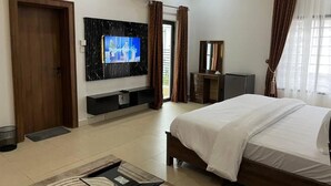 A modern hotel room with a large bed, a flat-screen TV mounted on the wall, a small desk, and a window with curtains. - O2 Contiential Suites  (Abuja)