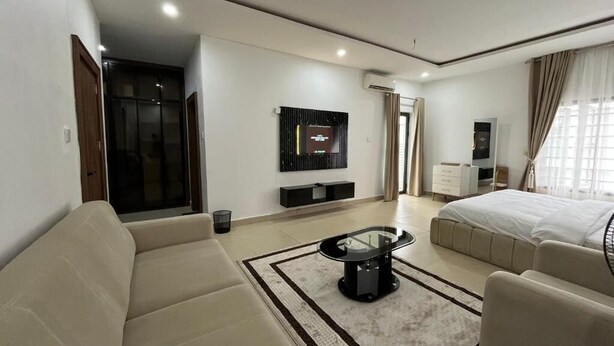 A modern hotel room with a sofa, a coffee table, a bed, a TV, and a wardrobe. - O2 Contiential Suites  (Abuja)