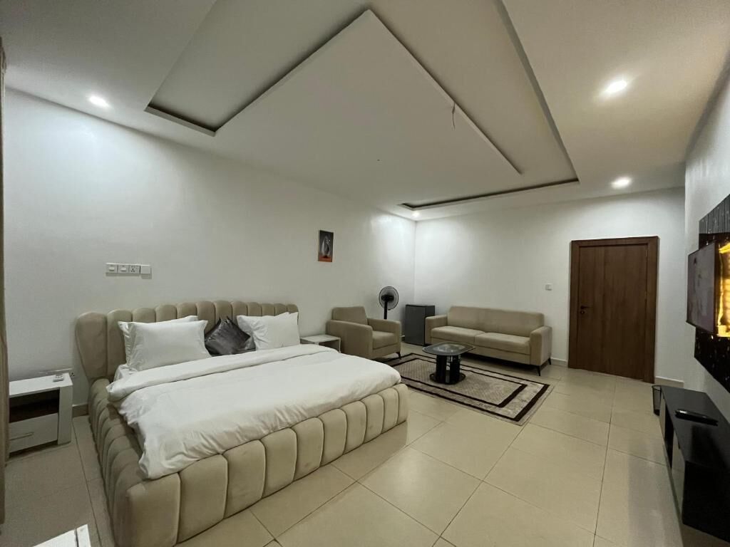 A modern bedroom with a large bed, a sofa, a TV, and a wooden door.