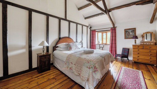 A bedroom with a wooden floor, a bed with a floral bedspread, a nightstand, a dresser, and a window with curtains. - 16th Century Devon Farmhouse, Stunning Views (Winkleigh)