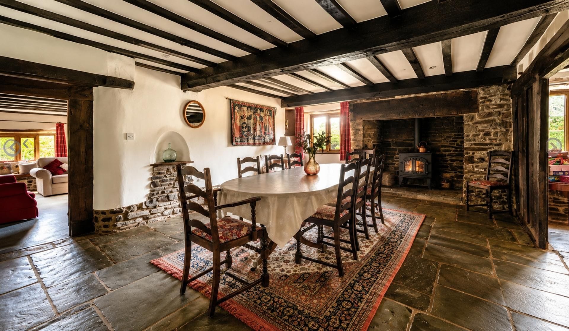 A traditional dining room with a stone fireplace, wooden beams, and a round table surrounded by chairs.