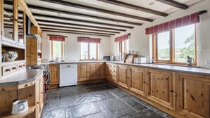 A kitchen with wooden cabinets, a stone floor, and a view of the outdoors through large windows. - 16th Century Devon Farmhouse, Stunning Views (Winkleigh)