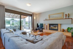 A modern living room with a sofa set, a TV, a fireplace, and a large window. - Villa Ampelaki (Chania)