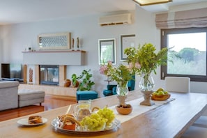 A dining area with a wooden table set with food, a fireplace, and potted plants. - Villa Ampelaki (Chania)