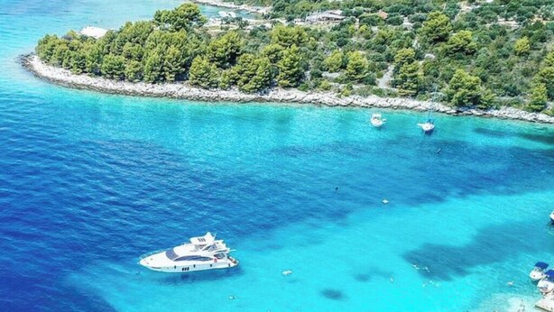 An aerial view of a coastal area with clear turquoise waters, a yacht anchored near the shore, and a small beach populated with people. - Apartments Mia with new whirlpool from 2026 and 7 minutes walk from the beach (Okrug Gornji)