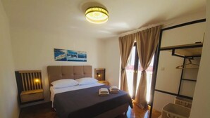 A bedroom with a bed, bedside tables, a hanging light fixture, a wardrobe, and a window with curtains. - Apartments Mia with new whirlpool from 2026 and 7 minutes walk from the beach (Okrug Gornji)