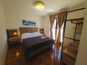 Ein Schlafzimmer mit Bett, Nachttischen, einer Hängelampe, einem Kleiderschrank und einem Fenster mit Vorhängen.