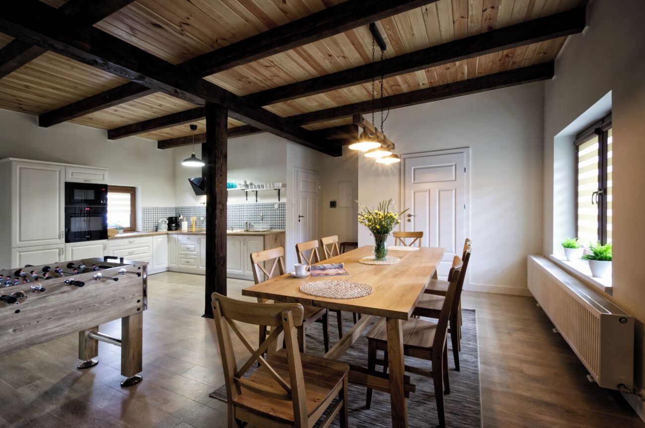 A spacious dining area with a wooden table and chairs, a foosball table, and a kitchen in the background.