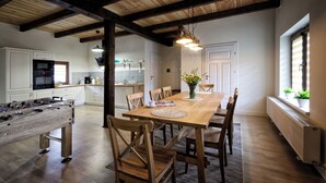 Un grand espace dédié à la salle à manger, avec une table et des chaises en bois, un baby-foot et une cuisine en arrière-plan.