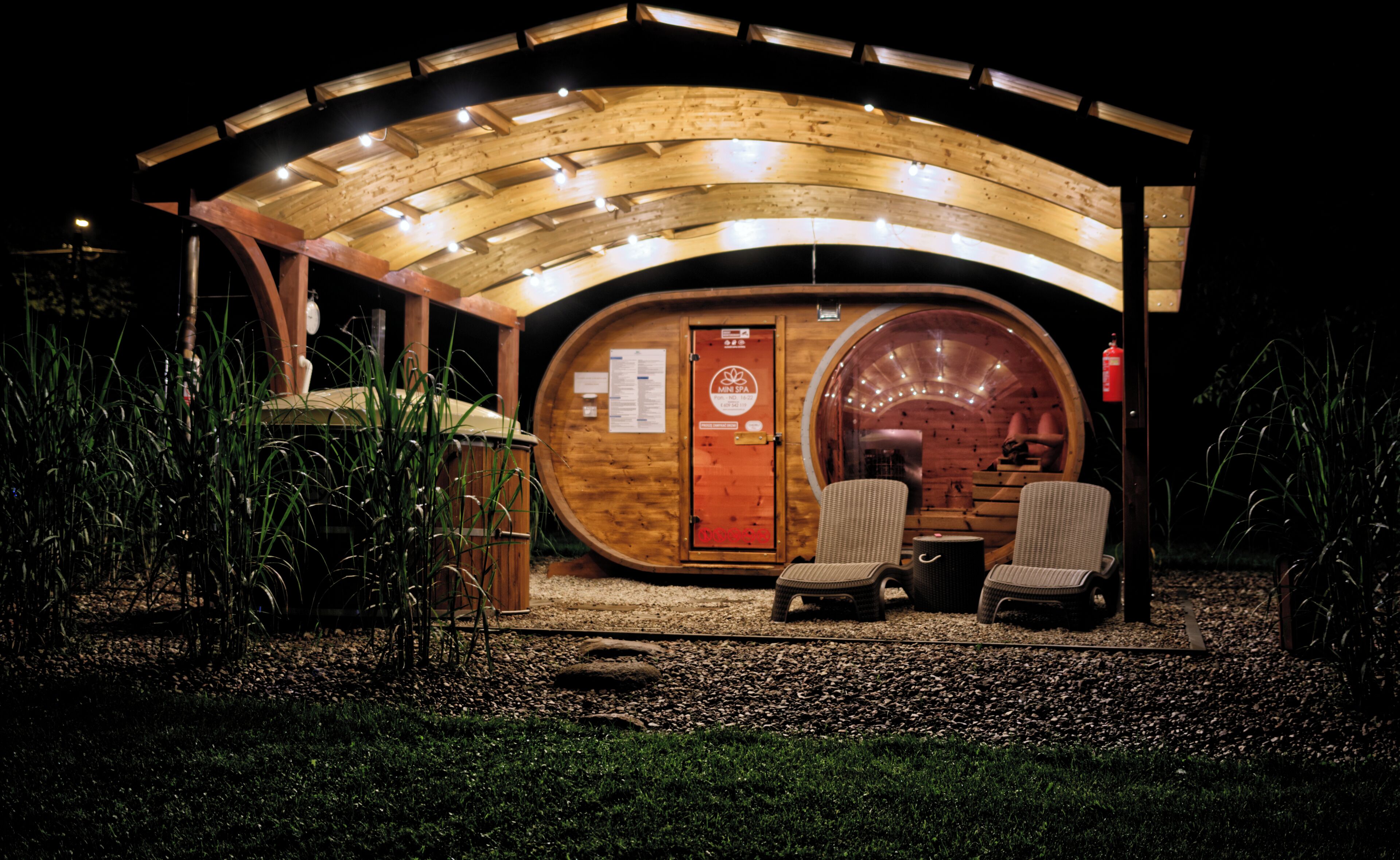 A wooden structure with a semi-circular roof, a door labeled 'MINI SPA', and two wicker chairs outside.