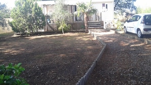 Una casa a un piano con veranda, un piccolo giardino con una palma e un'auto bianca parcheggiata nel vialetto.