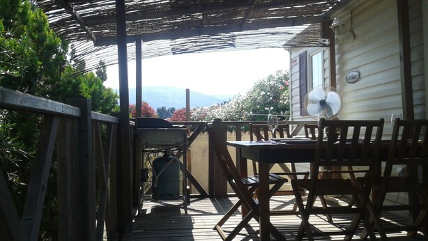 Un portico coperto con tavolo e sedie, una ventola e vista su una casa e montagne.
