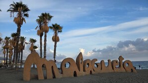 Une plage où se trouve une grande sculpture de sable représentant le mot « Malaga », avec des palmiers en arrière-plan.