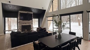 Un salón amplio con una chimenea grande, un sofá negro y un comedor con una mesa y sillas de madera oscura.