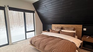Un dormitorio con una cama grande, cabecera de madera y vistas a un paisaje nevado a través de las ventanas.