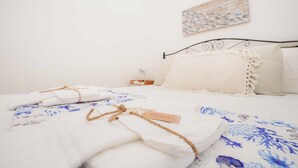A neatly made bed with folded towels and a tag, a white wall with a framed artwork, and a small bedside table with a lamp. - Poésia – Portuligno Apartment 50 mt from the most beautiful beaches in Salento! (melendugno)