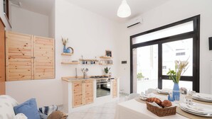 A modern kitchen with wooden cabinets, a built-in oven, and a dining area with a table set for two. - Poésia – Portuligno Apartment 50 mt from the most beautiful beaches in Salento! (melendugno)