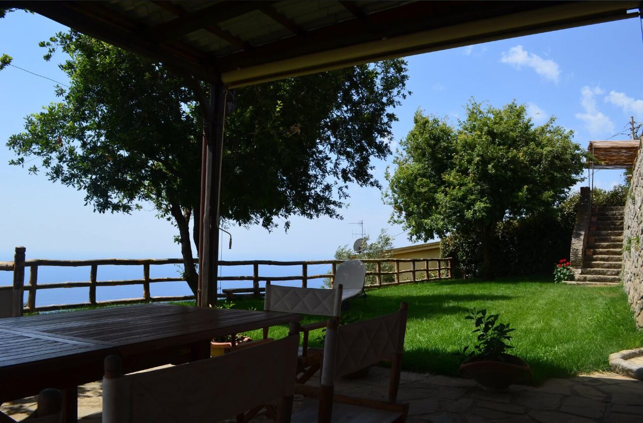 Un espace extérieur aménagé avec une table et des chaises, offrant une vue sur une étendue d’eau et un mur de pierre.
