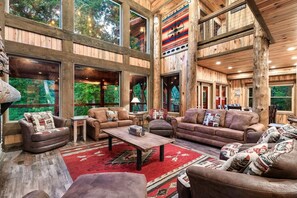 Ein großzügiger Innenraum mit großen Fenstern, Holzwänden und einer gemütlichen Sitzecke mit mehreren Sofas und einem Couchtisch.