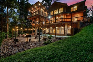 Una casa de madera de varios pisos, con balcón, mobiliario exterior e iluminada con luces colgantes.