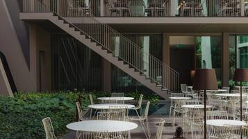 A modern outdoor dining area with round tables and chairs, a staircase, and a balcony with seating.