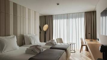 A hotel room with two beds, a desk, a chair, and a large window with curtains.