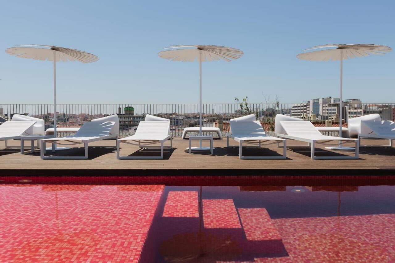 A poolside area with lounge chairs and umbrellas, a tiled pool, and a cityscape in the background.