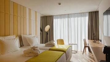 A hotel room with two beds, a desk, a chair, a small table, and a large window with curtains.