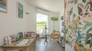 Una stanza con un tavolo da pranzo, due sedie in vimini, un piccolo tavolino con una pianta in vaso e una parete decorata con un grande murale botanico.