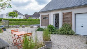 Un patio con ghiaia, un tavolo e sedie in legno, un edificio con un'autorimessa e un cartello che indica un ristorante.