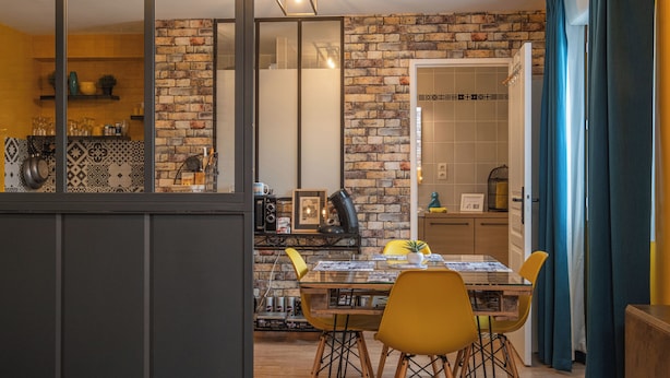 Una cucina moderna con parete in mattoni, mobili in legno e zona pranzo con sedie gialle e tavolo in vetro.