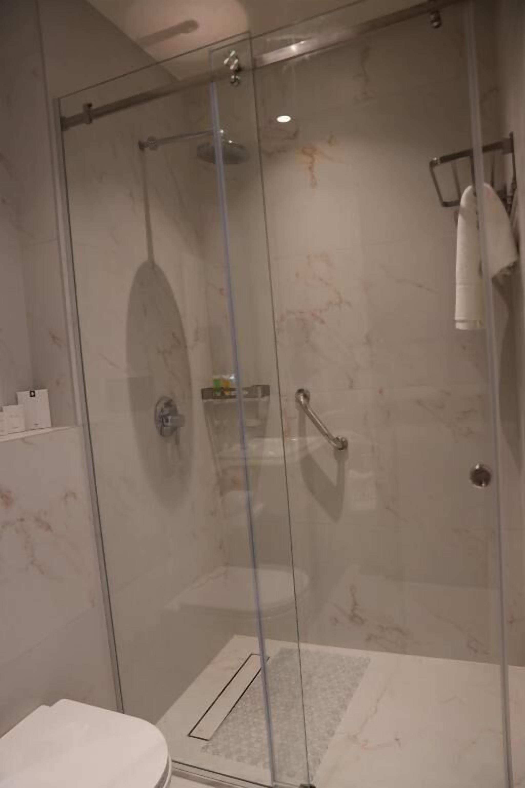 Un box de ducha con paredes de azulejos blancos, un perchero y un estante pequeño con artículos de aseo.