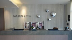 Ein Empfangsschalter mit Holzverkleidung, einem Namensschild mit der Aufschrift 'GOLDEN SUITES' und drei gerahmten Fotografien mit Blumenblumen.