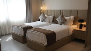 Ein Hotelzimmer mit zwei Betten, einem Nachttisch mit Lampe und einem Fenster mit Vorhängen.