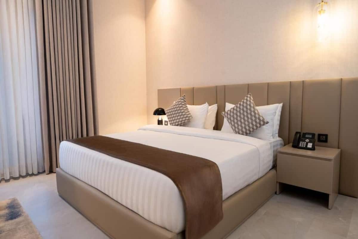 Una habitación de hotel con una cama grande, una mesita de noche con un teléfono y una lámpara de pared.