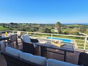 Una terraza con mobiliario de mimbre, una mesa de comedor y vistas a una piscina y al paisaje.