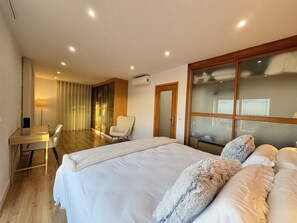 Ein modernes Hotelzimmer mit einem großen Bett, einem Schreibtisch, einem Stuhl und einer Glastür, die auf einen Balkon führt.