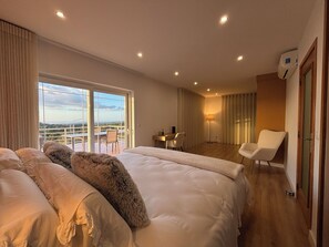 Ein modernes Hotelzimmer mit einem großen Bett, einem Schreibtisch und einem Stuhl. Ein Balkon bietet Blick auf die Landschaft.