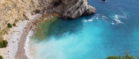 A coastal landscape with a rocky cliff and a clear blue sea.