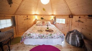 Ein gemütliches Schlafzimmer in einer Holzhütte mit einem Bett, einem kleinen Tisch und einem Fenster.