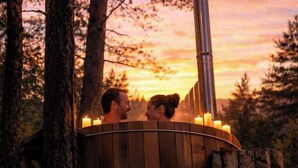 Ein hölzernes Whirlpool mit Kerzen, umgeben von Bäumen, während der Sonnenuntergang stattfindet.