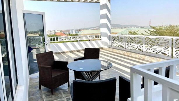 A balcony with wicker furniture and a glass door, overlooking a cityscape. - Marcopolo Hotel and Suites  (Lekki)