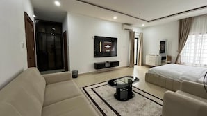 A modern hotel room with a sofa, a coffee table, a bed, a TV, and a wardrobe. - Marcopolo Hotel and Suites  (Lekki)
